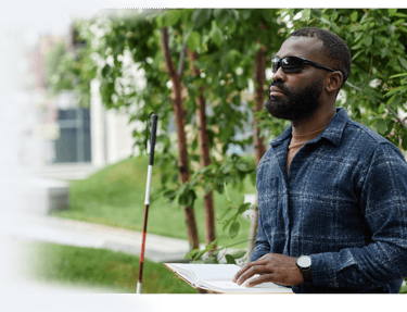 Man reading a Braille book in the park with his cane, highlighting accessible reading for the blind