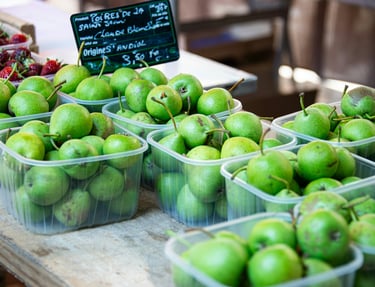Fresh green pears displayed in clear plastic punnets at a farmers market fresh produce packaging