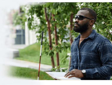 Man reading a Braille book in the park with his cane, highlighting accessible reading for the blind