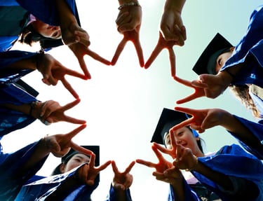 Group of graduates in blue gowns and caps forming a star shape with their fingers while celebrating 