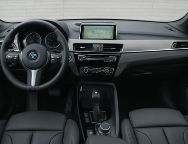 Interior do BMW X1 com volante, painel, tela central e console vistos de frente.