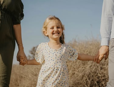 Fillette souriante en pleine nature, tenue par les mains de ses parents – photo de famille naturelle