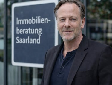 Professional real estate consultant standing by an Immobilienberatung Saarland sign.