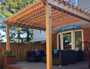 Wooden pergola built over a backyard deck with outdoor seating attached to a house.