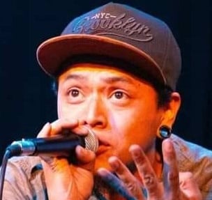 Un artista masculino de hip hop con una gorra snapback de Brooklyn, interpretando en un micrófono.