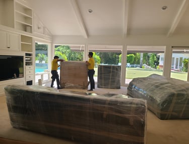 movers moving shrink-wrapped furniture inside a spacious living room during a residential move.