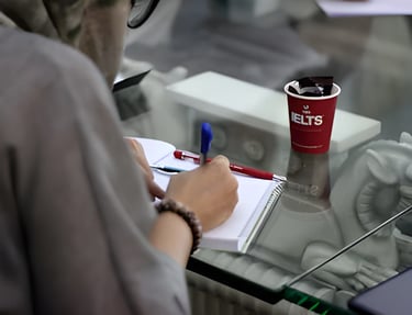 Person writing in a notebook, symbolizing IELTS preparation with U.E.L.T's cup for studying abroad