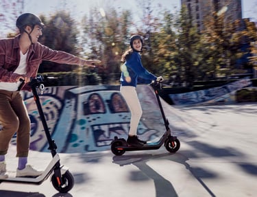 a man and woman riding scooters in a skateboard park