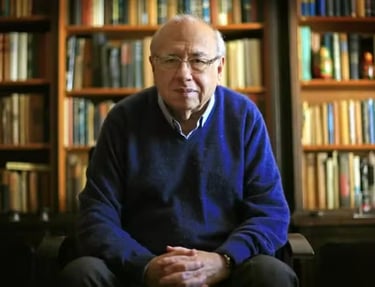 a man in a blue sweater and black pants sitting in front of a bookshel
