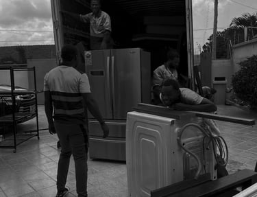 Black and white photograph of three movers efficiently loading large appliances into the open rear o