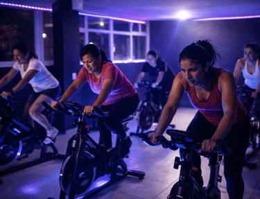 Grupo diverso de mujeres en una clase de spinning de alta intensidad con luces de neón violetas.