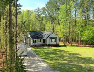 Scenic aerial view of a house with a lawn and gravel driveway surrounded by tall pine trees.