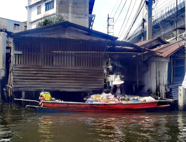 A local vendor in a small wooden boat selling goods at a Bangkok floating market canal.