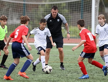 A group of smiling children eagerly playing soccer on a bright, sunny field surrounded by green trees.