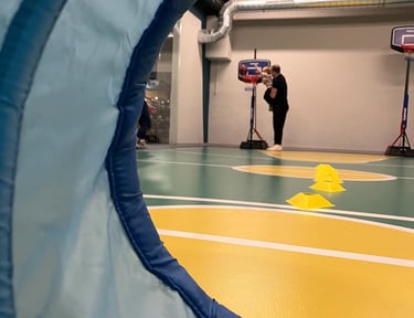 Vista attraverso un tunnel morbido in un'area multisport della palestra Move 2 Grow a Milano, con un adulto che aiuta un bamb