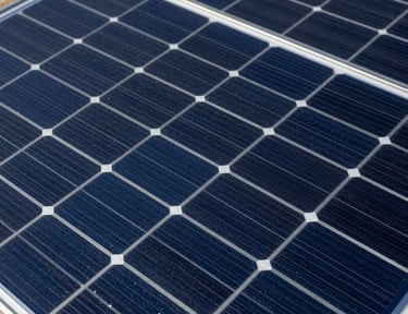 Close-up overhead shot of monocrystalline solar panel surface, blue-black cell grid with silver busbars, studio strobe lighting revealing precise cell geometry and anti-reflective coating texture
