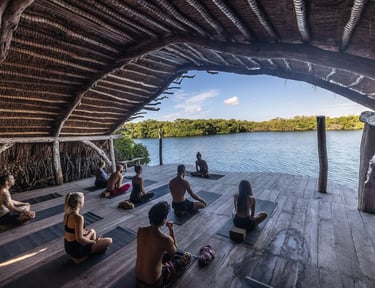 People practicing yoga in a wooden pavilion overlooking a serene lake during a yoga retreat.