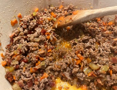 Browning ground beef with diced carrots and onions in a pot for a homemade bolognese sauce recipe.