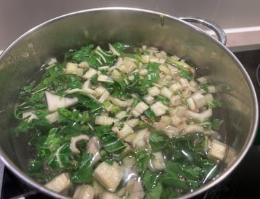 Fresh chopped bok choy simmering in a stainless steel pot of water for a healthy vegetable soup.