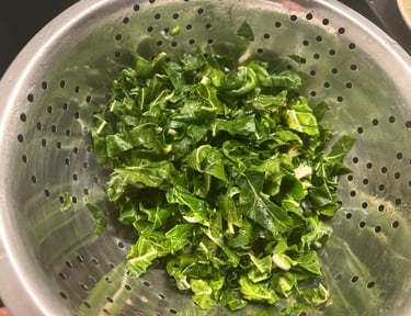 Freshly chopped green leafy vegetables being washed in a stainless steel kitchen colander.