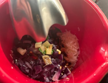 Mixing chopped red onions and pine nuts in a red bowl with an immersion blender to make pesto.