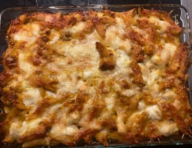 Golden brown baked penne pasta casserole topped with melted mozzarella cheese in a glass baking dish.