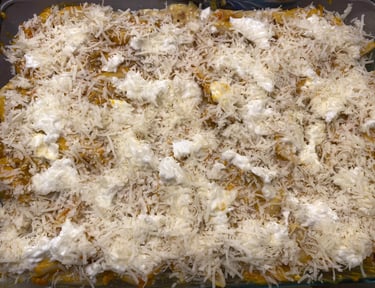 Homemade baked pasta dish topped with layers of shredded mozzarella and ricotta cheese in a glass pan.
