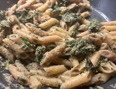 Healthy whole grain penne pasta tossed with fresh green spinach pesto sauce in a skillet.