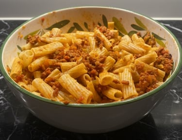 A ceramic bowl filled with rigatoni pasta tossed in a hearty meat bolognese sauce on a black marble surface.