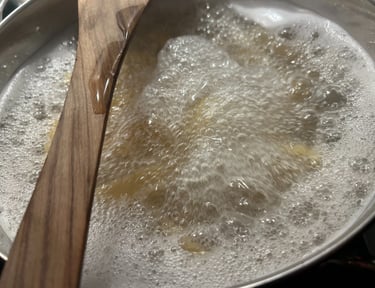 A wooden spoon resting on a stainless steel pot of rapidly boiling water and pasta noodles.