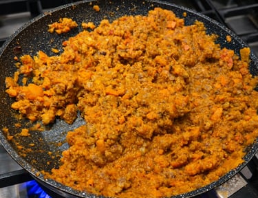 Hearty homemade bolognese sauce with ground meat and diced carrots simmering in a non-stick frying pan.