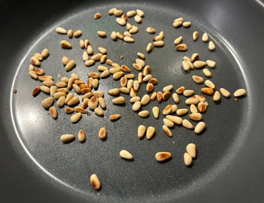 Golden toasted pine nuts scattered in a dark non-stick frying pan for cooking.