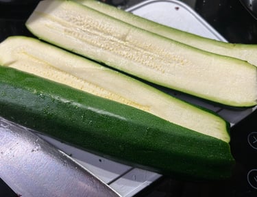 Fresh green zucchini sliced lengthwise on a white cutting board for meal prep and healthy cooking.