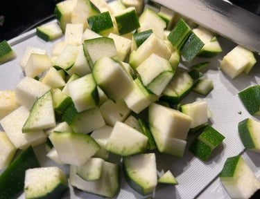 Fresh diced green zucchini pieces on a white cutting board for healthy meal preparation.