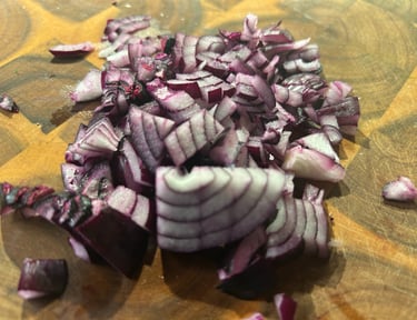 Finely diced red onion pieces on a wooden cutting board for meal prep and cooking.