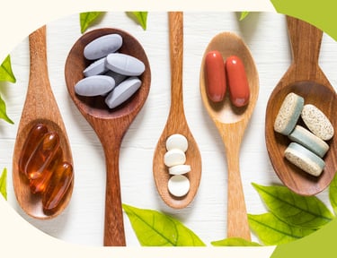 Variety of dietary supplements, vitamins, and herbal capsules on wooden spoons with green leaves.