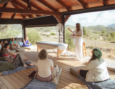 Sheila Doerfler in white linen explaining what a group biofield tuning session is to 9 people seated in Spanish country side