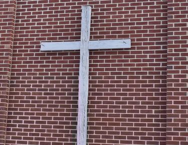 wooden cross hanging on a brick wall 