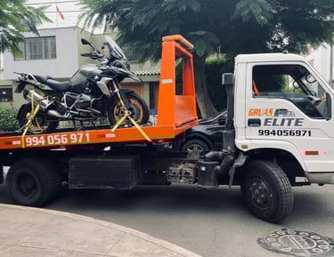 Camión grúa de plataforma transportando una moto de alto cilíndrale en una avenida urbana de Lima