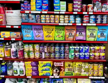 Round Hill Market shelf with pet foods, cleaning supplies, and household items including Ziploc bags and bath tissue.