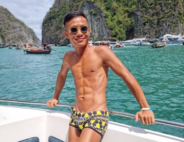 A male outcall masseur in pattaya standing on a boat wearing swim wear with the sea and an island in the background