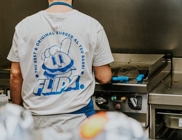Cocinero de Flipa en cocina con camiseta de la marca mientras prepara burgers a la plancha