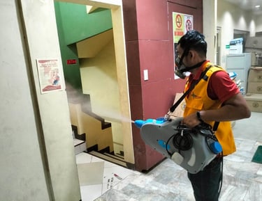 Professional pest control technician spraying disinfectant mist in an office building hallway.