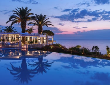 Luxury infinity pool reflecting palm trees and a sunset sky at Sani resort restaurant.