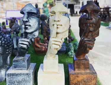 Three silence statues in silver, white, and bronze finishes holding a finger to their lips.
