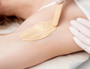 Professional esthetician applying warm sugar wax to a woman's underarm for hair removal.