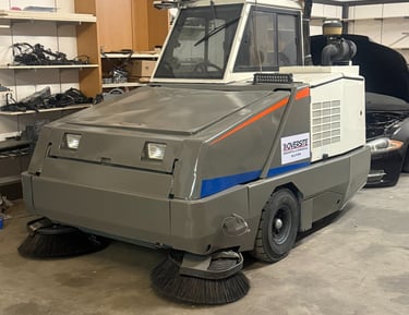 Industrial power sweeper machine for parking lot and warehouse floor cleaning in a garage.