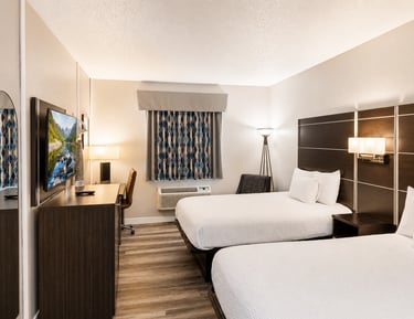 Modern hotel room with two queen beds, dark wood furniture, and a flat-screen TV.