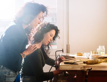 Dos artesanas trabajando juntas en un banco de madera en un taller de joyería.