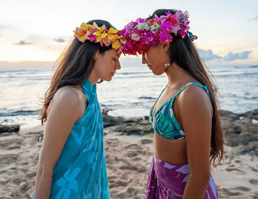 Two women with flower crowns sharing a moment of connection at the ocean during a Hawaiian retreat f